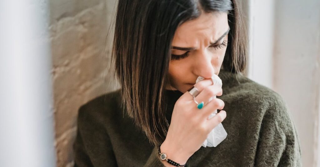 Despaired female with dark hair in casual clothes standing near wall with tissue in hand in light room at home